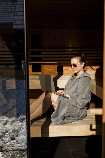 Woman sits with laptop in the sauna