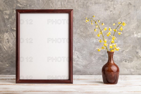 Wooden frame with yellow barrenwort flowers in ceramic vase on gray concrete background. side view, copy space, still life, mockup, template, spring, summer minimalism concept