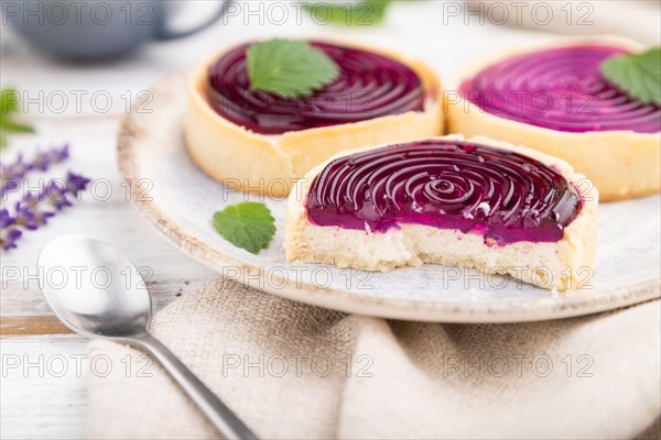 Sweet tartlets with jelly and milk cream with cup of coffee on a white wooden background and linen textile. Side view, close up, selective focus