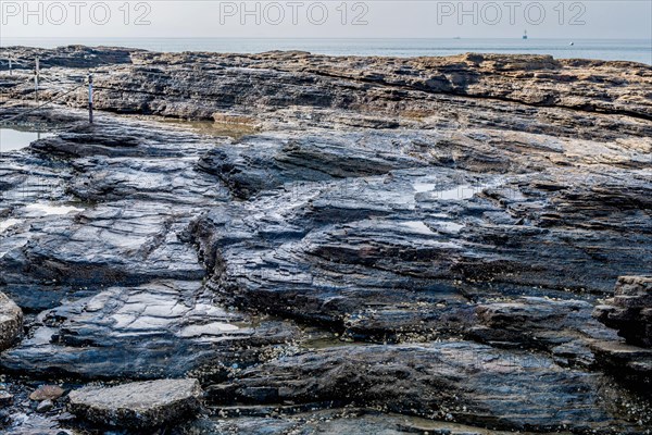 Stratified geological rocks with layers of various shapes with ocean in background in South Korea