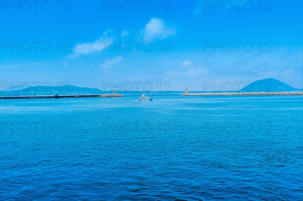 Fishing boat in front of harbor breakwater between two yellow lighthouses in Jeju, South Korea, Asia