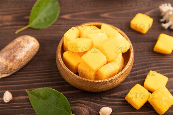 Dried and candied mango cubes in wooden bowls on brown wooden textured background. Side view, close up, selective focus, vegan, vegetarian food concept