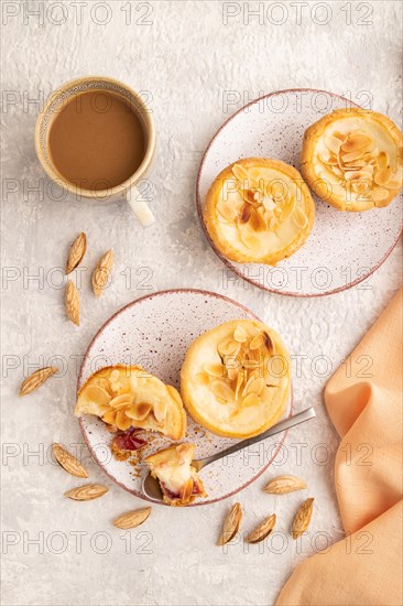 Traditional portuguese cakes pasteis de nata, custard small pies with almonds with cup of coffee on gray concrete background and orange textile. Top view, flat lay, close up