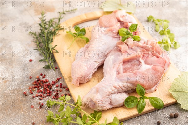 Raw turkey wing with herbs and spices on a wooden cutting board on a brown concrete background. Side view, close up, selective focus