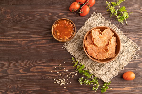 Slices of dehydrated salted meat chips with herbs and spices on brown wooden background and linen textile. Top view, flat lay, copy space