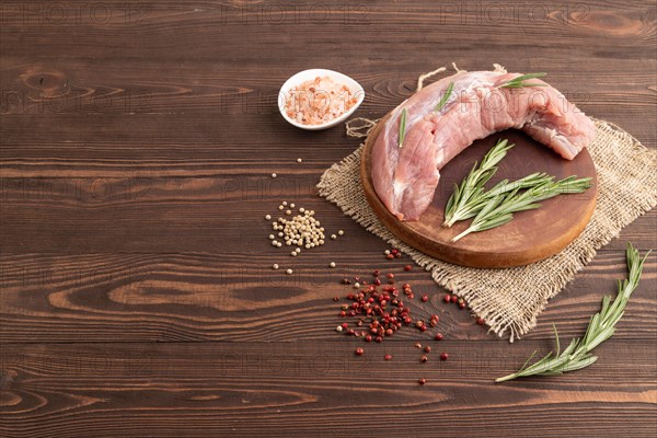 Raw pork with herbs and spices on a wooden cutting board on a brown wooden background. Side view, copy space