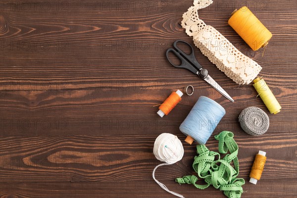 Sewing accessories: scissors, thread, thimbles, braid on brown wooden background. Top view, flat lay, copy space