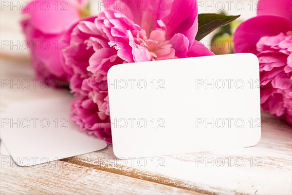 White business card with pink peony flowers on white wooden background. side view, copy space, still life. Breakfast, morning, spring concept