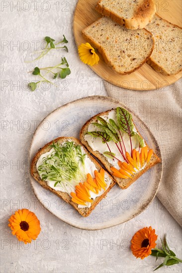 White bread sandwiches with cream cheese, calendula petals and microgreen on gray concrete background and linen textile. top view, flat lay, close up