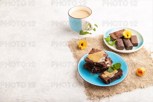 Chocolate brownie with caramel sauce with a cup of coffee on gray concrete background and linen textile. side view, copy space