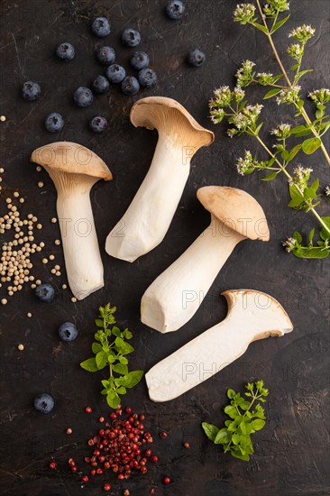 King Oyster mushrooms or Eringi (Pleurotus eryngii) on black concrete background with blueberry, herbs and spices. Top view, flat lay