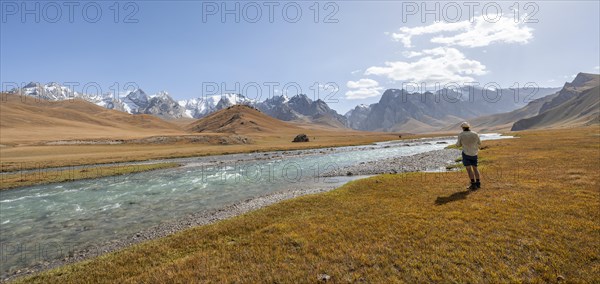 Mountaineer hiking to the mountain lake Kol Suu, mountain landscape with yellow meadows, river Kol Suu and mountain peaks with glacier, Keltan Mountains, Sary Beles Mountains, Tien Shan, Naryn Province, Kyrgyzstan, Asia