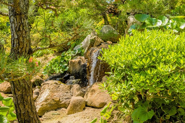 Small waterfall behind shrubbery in Japanese garden park in Hiroshima, Japan, Asia
