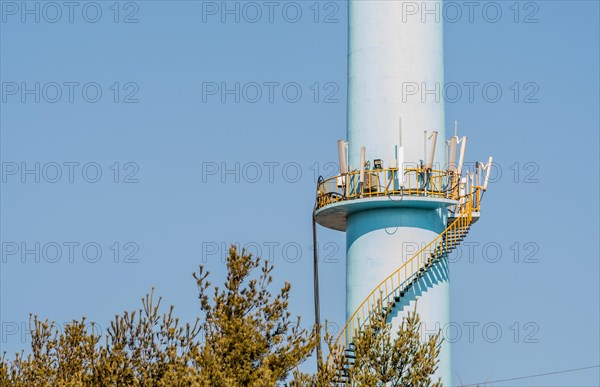 Closeup of spiral staircase leading to cellphone transmission array on tall concrete column with blue sky in background