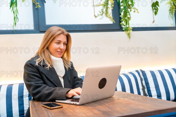 Elegant adult blonde woman working with laptop sitting in a colorful cafeteria