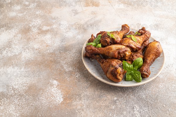 Smoked chicken legs with herbs and spices on a ceramic plate on a brown concrete background. Side view, copy space