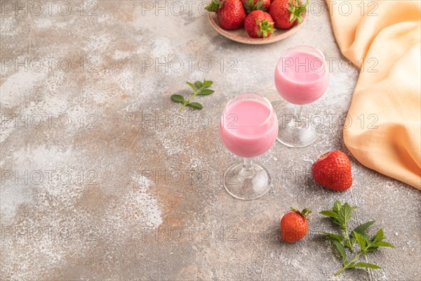 Sweet strawberry liqueur in glass on a gray concrete background and orange textile. side view, copy space