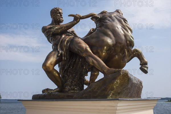 Bronzed cast zinc sculpture, statue, Heracles, taming the Cretan bull, artist: August Kriesmann, castle garden at Schwerin Castle, Schwerin's inner lake in the background, summery blue sky with light clouds, Schwerin, Mecklenburg-Western Pomerania, Germany, Europe