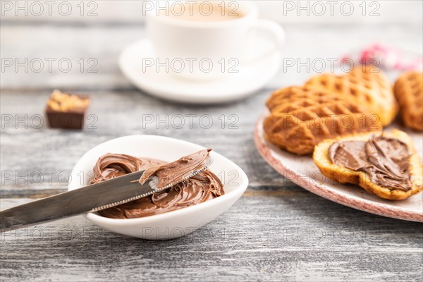 Homemade waffle with chocolate butter and cup of coffee on a gray wooden background. side view, selective focus, close up