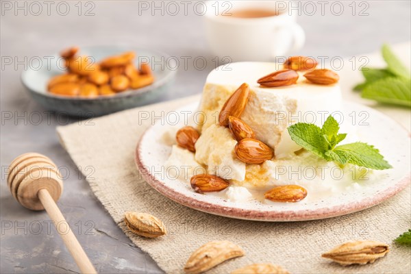 Ricotta cheese with honey and almonds on gray concrete background and linen textile. side view, close up, selective focus