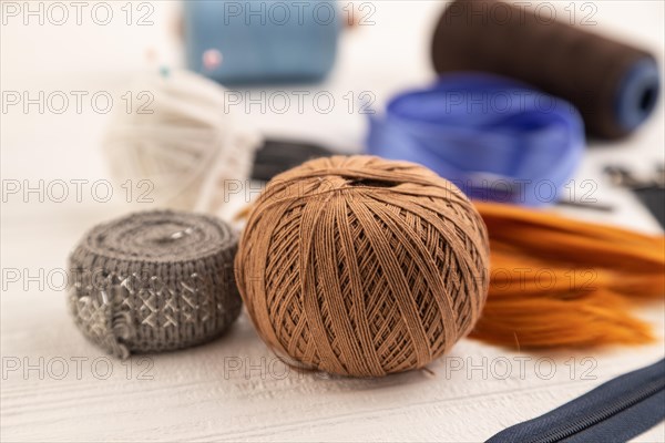 Sewing accessories: scissors, thread, thimbles, braid on white wooden background. Side view, close up, selective focus