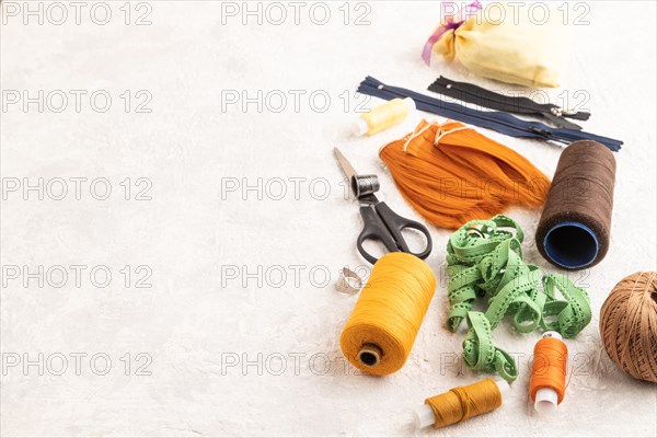 Sewing accessories: scissors, thread, thimbles, braid on gray concrete background. Side view, copy space