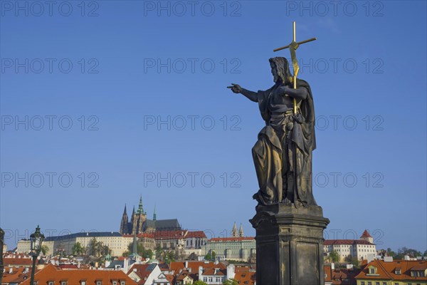 Statue of St. John the Baptist on Charles Bridge, with Hradcany castle and St. Vitus Cathedral in the background, in Prague, Czech Republic, in sunny day, Europe