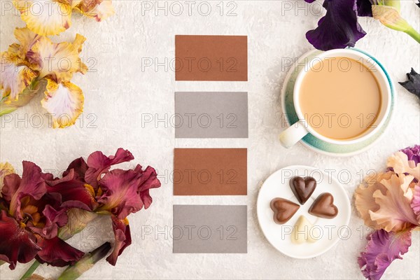 Set of gray and brown business cards with cup of cioffee, chocolate candies, purple and burgundy iris flowers on gray concrete background. top view, flat lay, copy space, still life. Breakfast, morning, spring concept