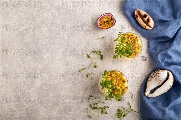 Yogurt with passionfruit and marigold microgreen in glass on gray concrete background with blue linen textile. Top view, flat lay, copy space