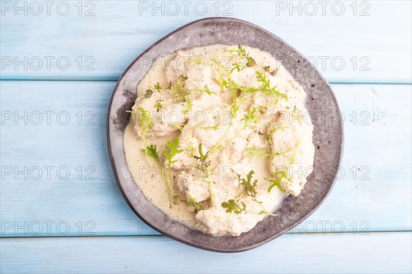 Stewed chicken fillets with coconut milk sauce and mizuna cabbage microgreen on blue wooden background. top view, flat lay, close up