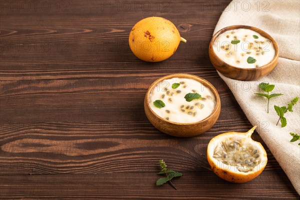 Yoghurt with granadilla and mint in wooden bowl on brown wooden background and linen textile. side view, copy space