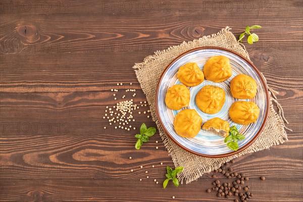 Fried manti dumplings with pepper, basil on brown wooden background and linen textile. Top view, flat lay, copy space