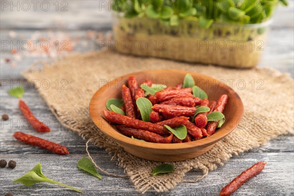 Small smoked sausage with borage microgreen, salt and pepper on gray wooden background and linen textile. Side view, close up, selective focus