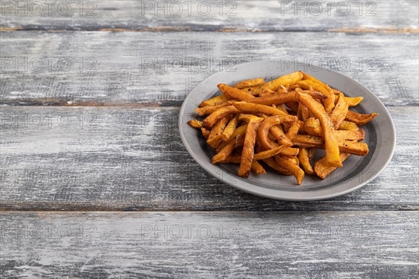 Heap of fried potato on a gray plate on a gray wooden background. Side view, close up, copy space