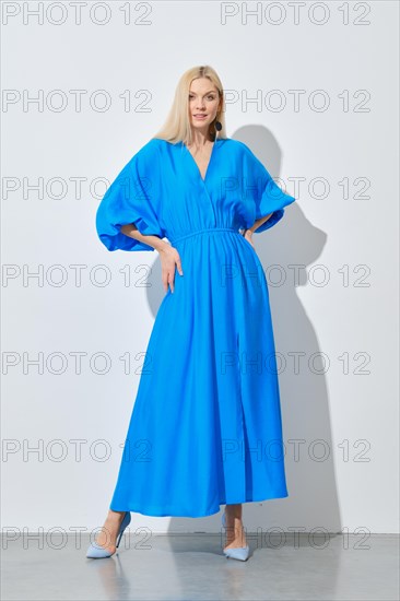 A stylish woman with long blonde hair posing in a vibrant blue dress
