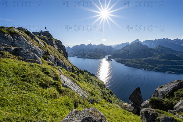 Mountaineer on the summit of Dronningsvarden or Stortinden, behind sea and fjord Umvagsundet, Sonnenstern, Vesteralen, Norway, Europe