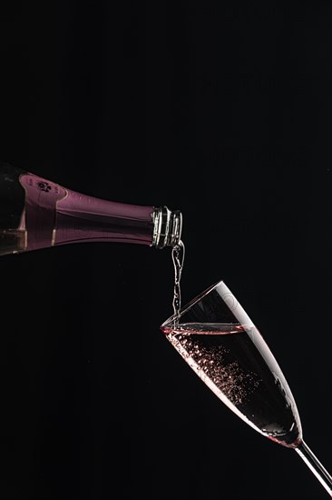 Pink champagne is poured into a slanted glass against a black background