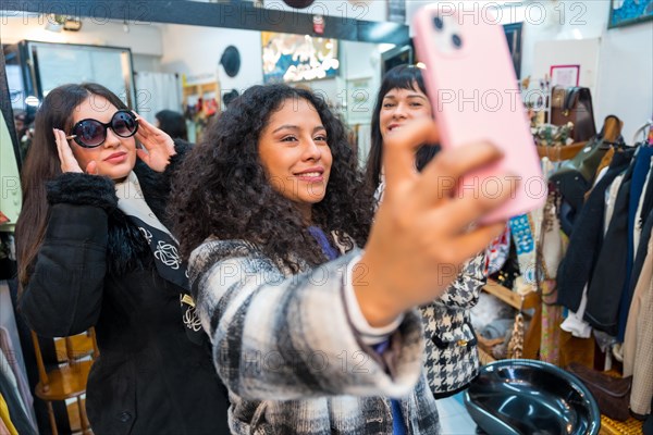 Frontal view of three beauty female friends taking fun selfie while trying on clothes during sales