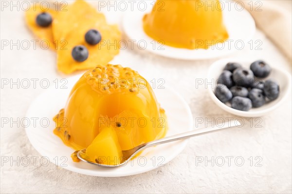 Mango and passion fruit jelly with blueberry on gray concrete background and linen textile. side view, close up, selective focus