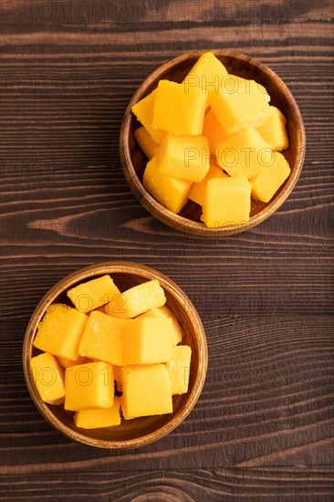 Dried and candied mango cubes in wooden bowls on brown wooden textured background. Top view, flat lay, close up, vegan, vegetarian food concept