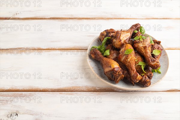 Smoked chicken legs with herbs and spices on a ceramic plate on a white wooden background. Side view, copy space
