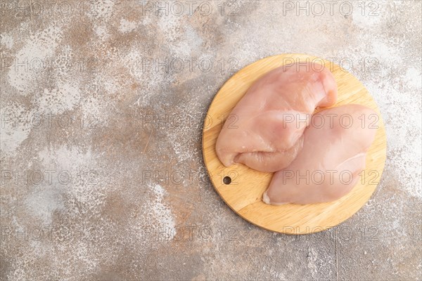 Raw chicken breast on a wooden cutting board on a brown concrete background. Top view, flat lay, copy space
