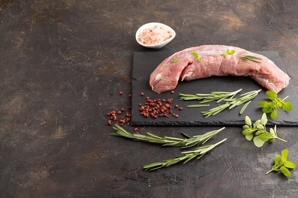 Raw pork meat with herbs and spices on slate cutting board on black concrete background. Side view, copy space