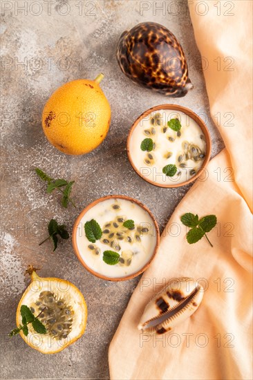Yoghurt with granadilla and mint in clay bowl on brown concrete background and orange linen textile. top view, flat lay, close up