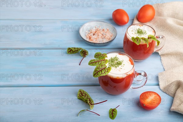 Tomato juice with sorrel, himalayan salt and sour cream in glass on blue wooden background with linen textile. Healthy drink concept. Side view, copy space