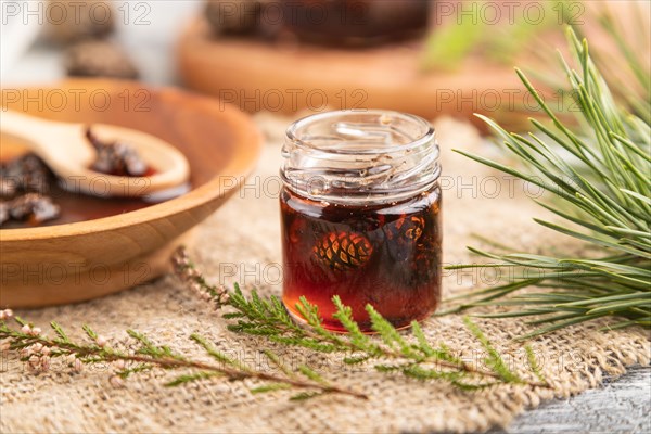 Pine cone jam with herbal tea on gray wooden background and linen textile. Side view, close up, selective focus