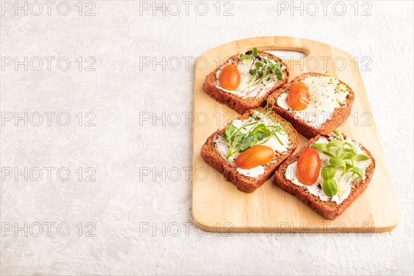 Red beet bread sandwiches with cream cheese, tomatoes and microgreen on gray concrete background. side view, copy space