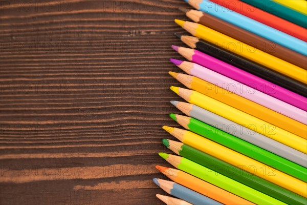 Set of watercolor pencils on brown wooden background. Top view, flat lay, copy space