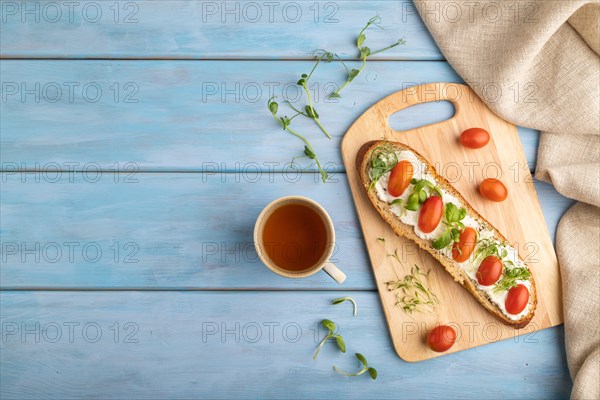 Long white bread sandwich with cream cheese, tomatoes and microgreen on blue wooden background and linen textile. top view, flat lay, copy space