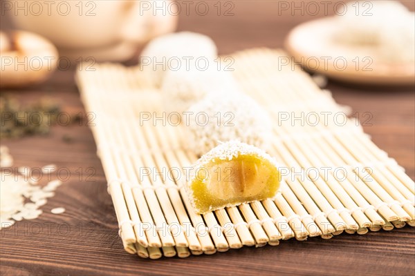 Japanese rice sweet buns mochi filled with pandan and coconut jam and cup of green tea on brown wooden background. side view, close up, selective focus